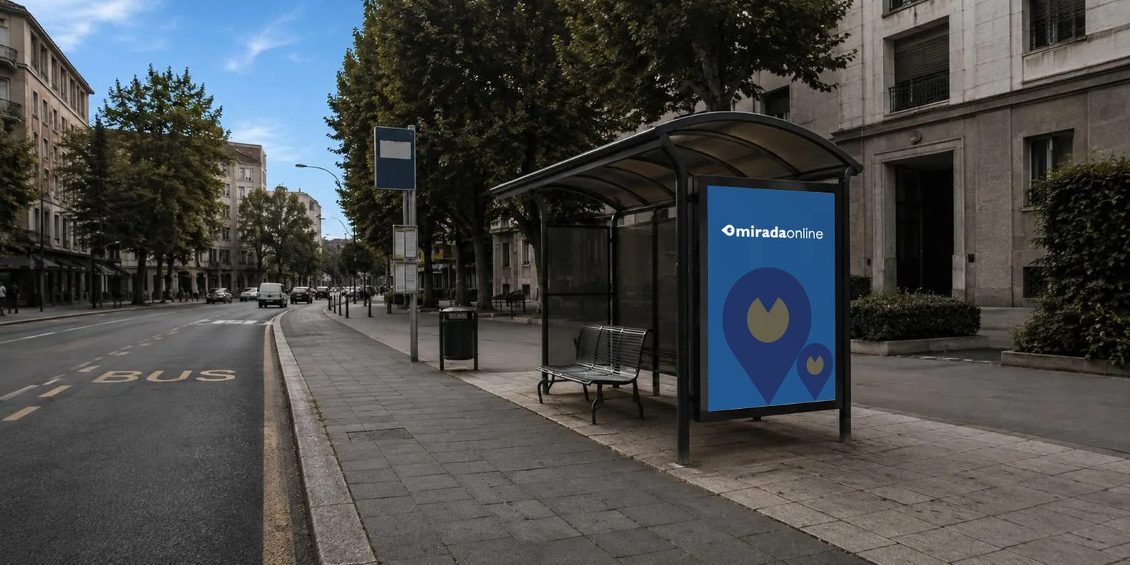 Una pensilina di attesa dell'autobus su un viale cittadino: sul poster blu c'è il logo MiradaOnline, in alto, sopra due segnaposto.
